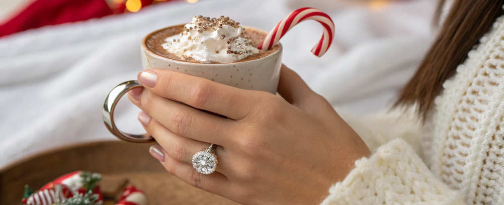 Engagement ring on a woman's hand holding a cup of hot cocoa. 